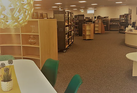 Blick in das Foyer der Bücherei mit hözernen mit Büchern gefüllten Regalelementen Ecke Tisch mit Blick in die Stadtbücherei