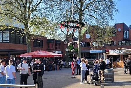 Menschen zwischen Buden und Maibaum auf dem Marktplatz Wahlstedt